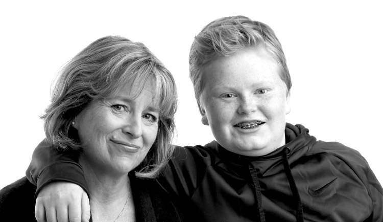 Both Suzanne and her son smile for the camera and her son's arm rests on her shoulders.