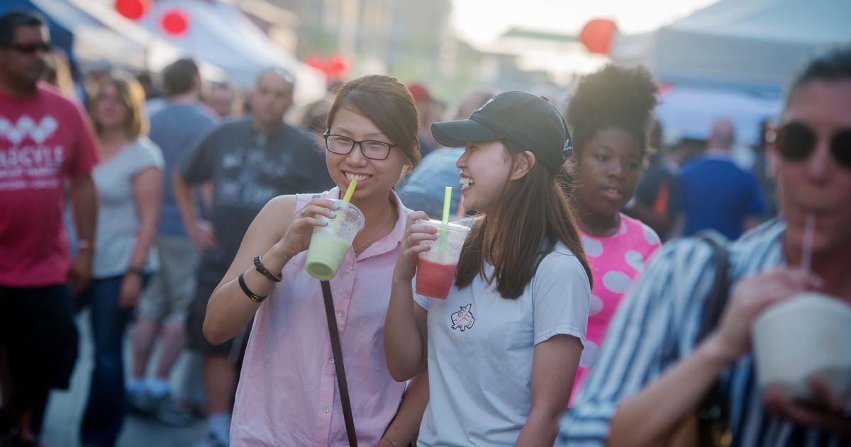 Two women smile while drinking smoothies at outdoor event