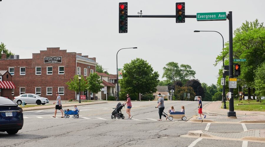 Adult with child in wagon, adult with stroller, adult with two children in wagon, and boy cross at an intersection