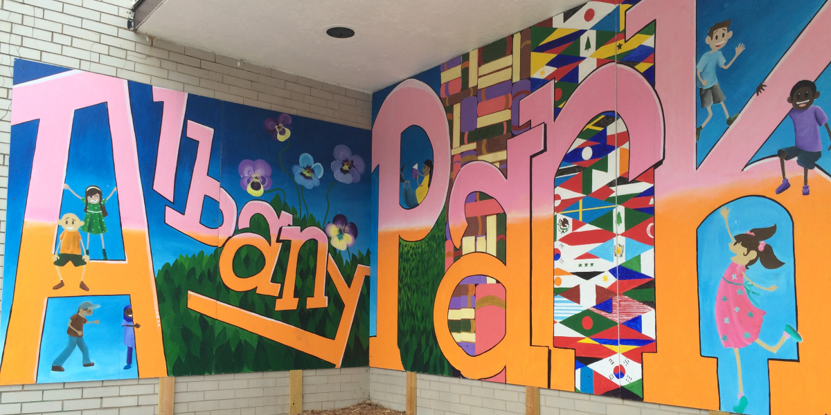 Mural with words "Albany Park" and flowers, children, books, and many different flags painted