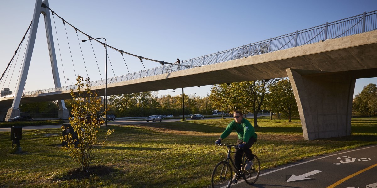 Pedestrian bridge over bike path and highway. Person biking