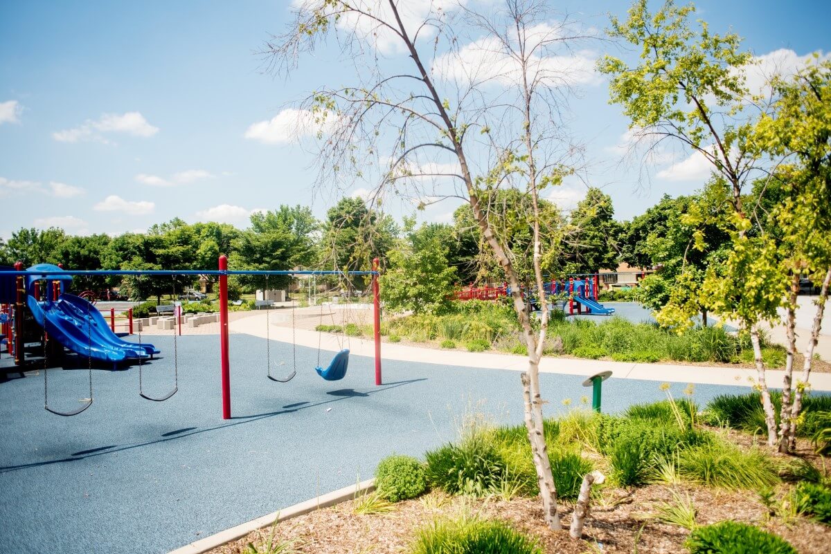 Playground swingset and slides next to garden areas