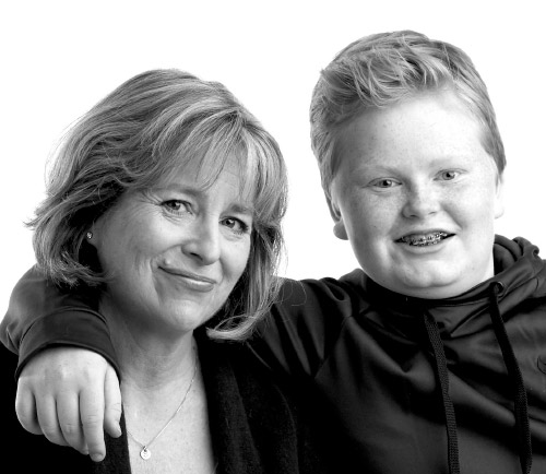 Both Suzanne and her son smile for the camera and her son's arm rests on her shoulders.